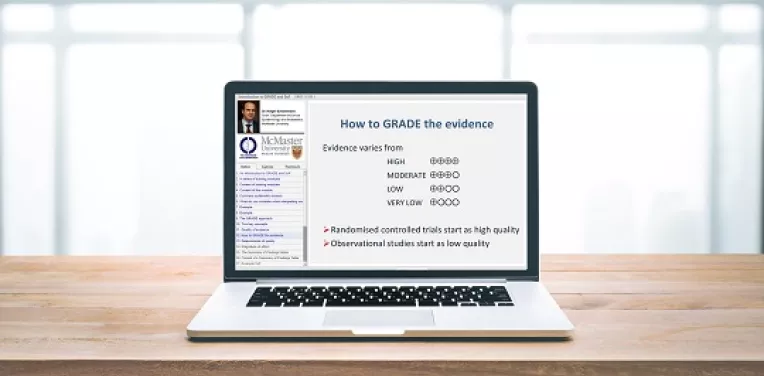 A laptop with a slide showing 'How to GRADE' the evidence on the screen