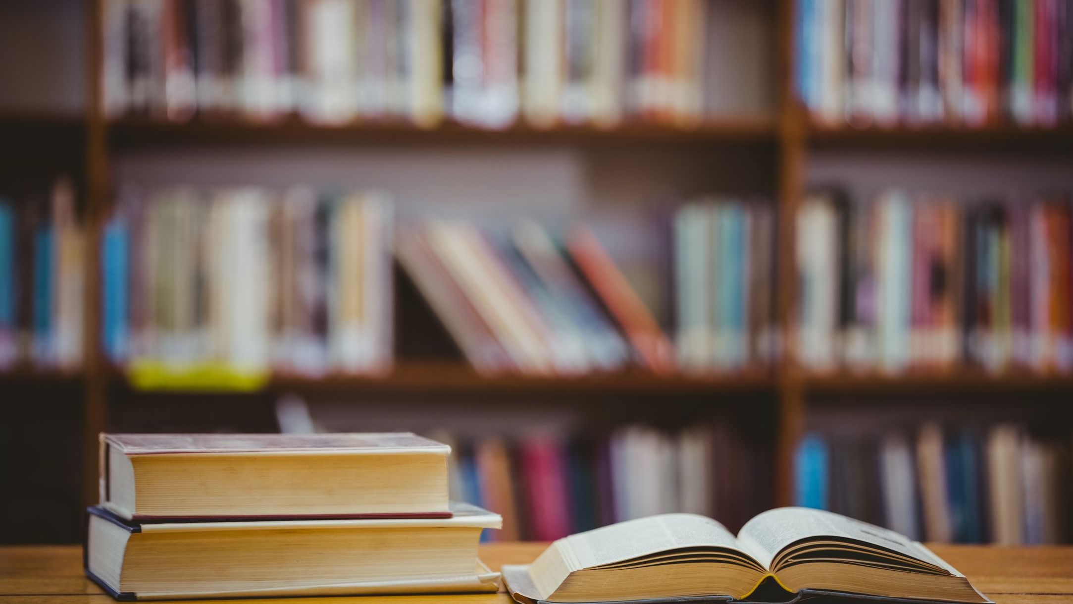Two books neatly stacked on desk, next to one book open